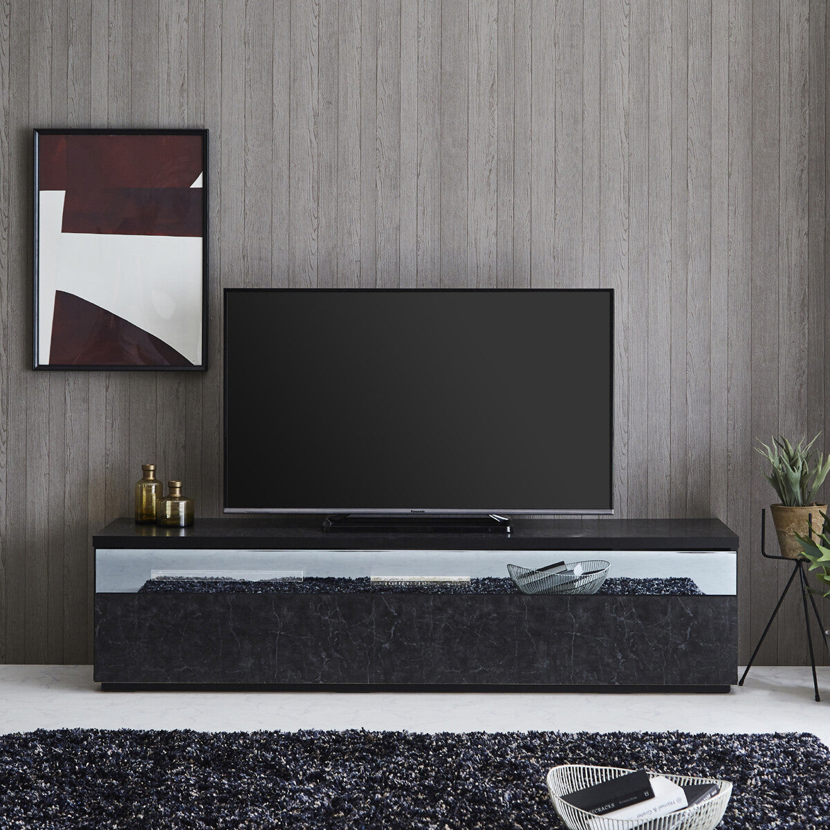 ストーンブラックのテレビボードに薄型テレビを置いた使用イメージ。石目調の前板と横長の光沢パネルを、グレーの壁や黒いラグと合わせたリビング