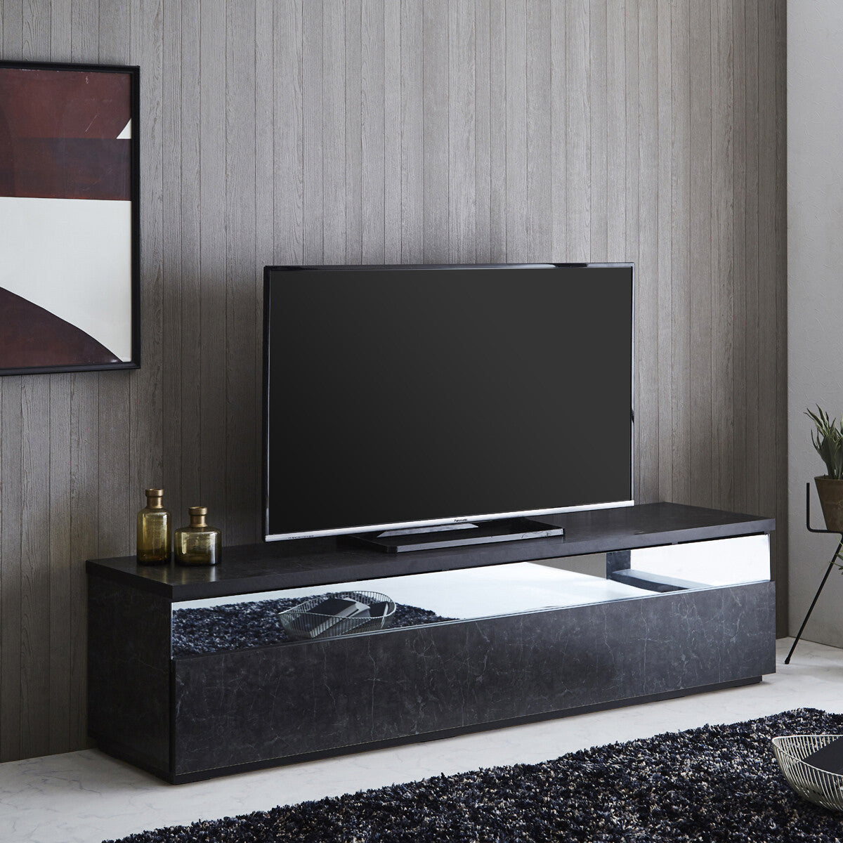 ブラック系の石目調テレビボードを斜め前から見た使用イメージ。薄型テレビを置き、横長の光沢パネルと側面が見えるデザイン