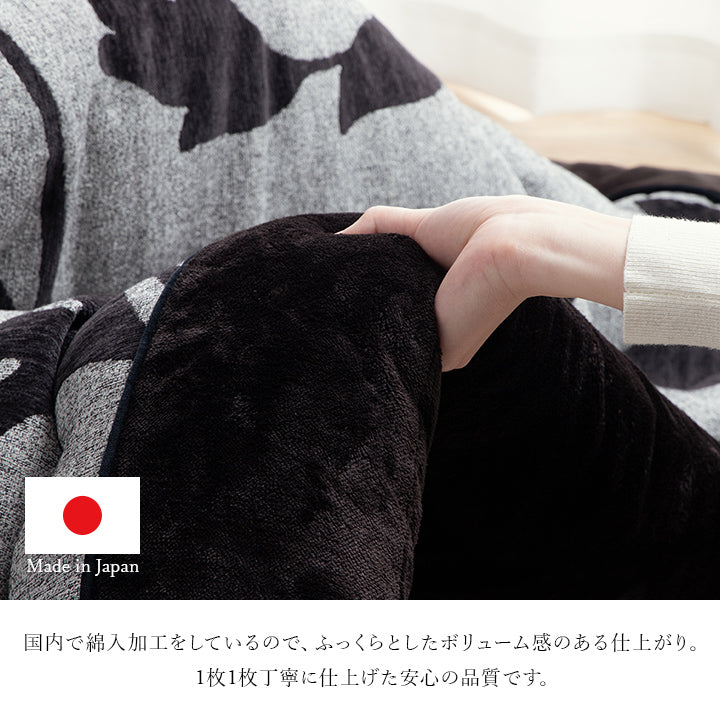 リーフ柄こたつ掛け布団の黒い縁を手で持ち、国内綿入れ加工によるふっくらした厚みを示した画像
