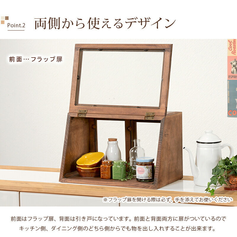 ブラウンの木製カウンター上ガラスケースの前面フラップ扉を開いた様子。背面には引き戸があり、両側から食器や小物を出し入れできる構造