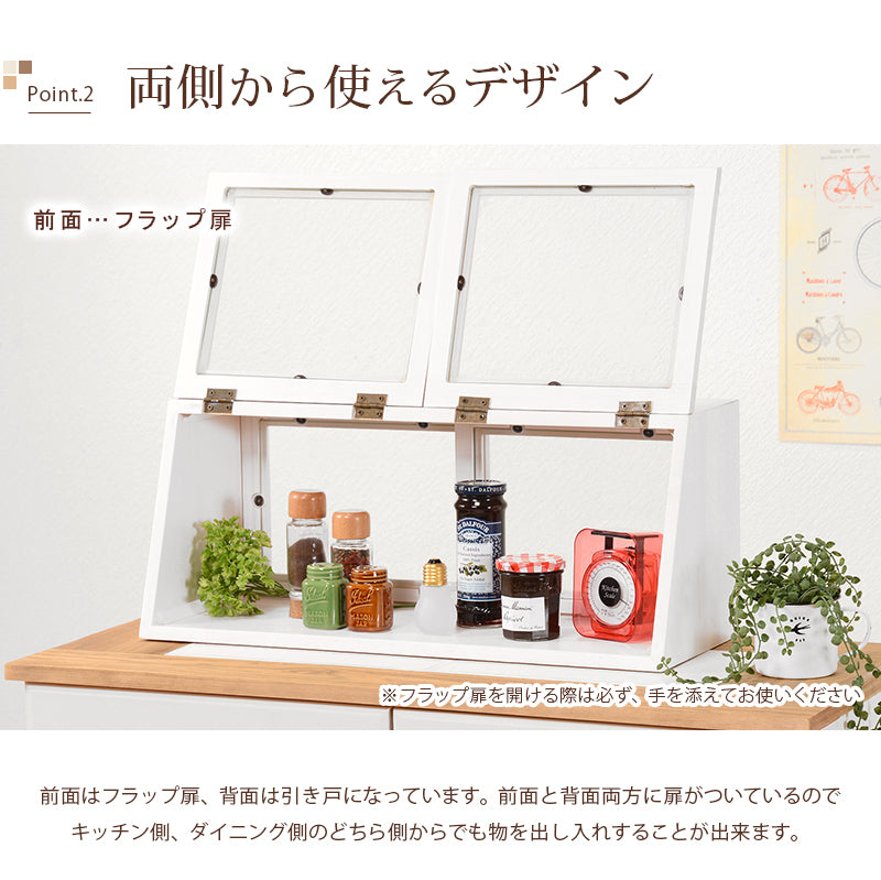 ウォッシュホワイトの横長木製カウンター上ガラスケース。左右の前面フラップ扉を開き、調味料や瓶、小物を並べた収納例