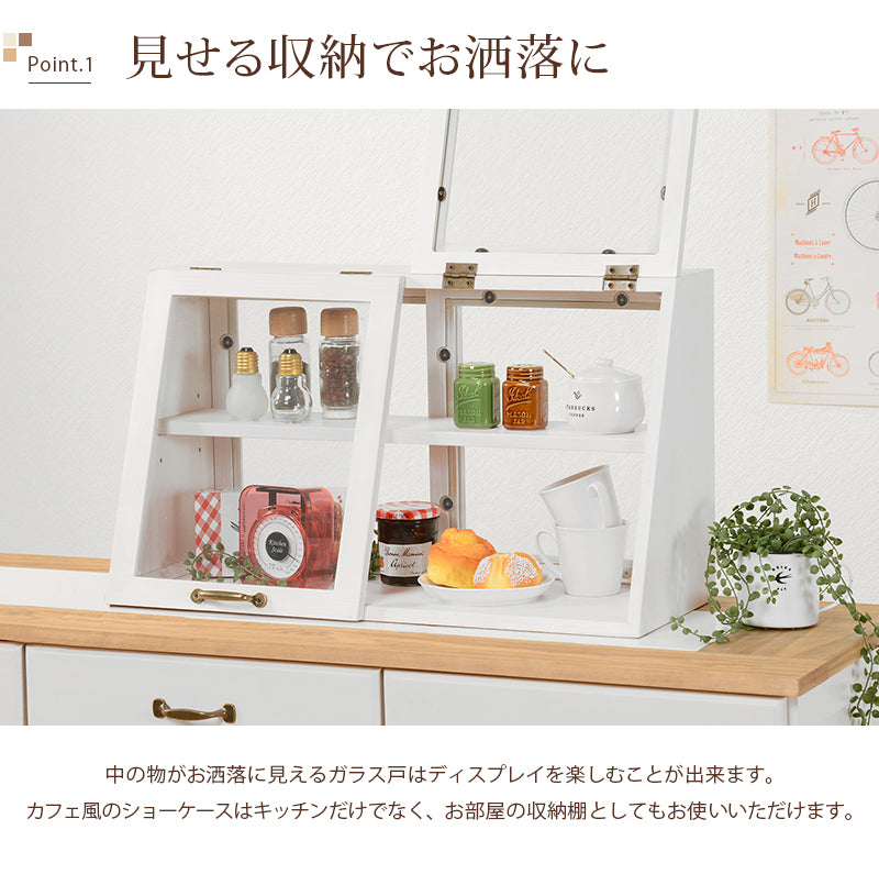 ウォッシュホワイトの横長木製カウンター上ガラスケース、2段タイプ。右側の前面フラップ扉を開き、上下の棚に調味料や食器、小物を並べた収納例