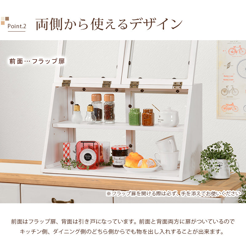 ウォッシュホワイトの横長木製カウンター上ガラスケース、2段タイプ。左右の前面フラップ扉を開き、上下の棚に調味料や食器、小物を並べた収納例